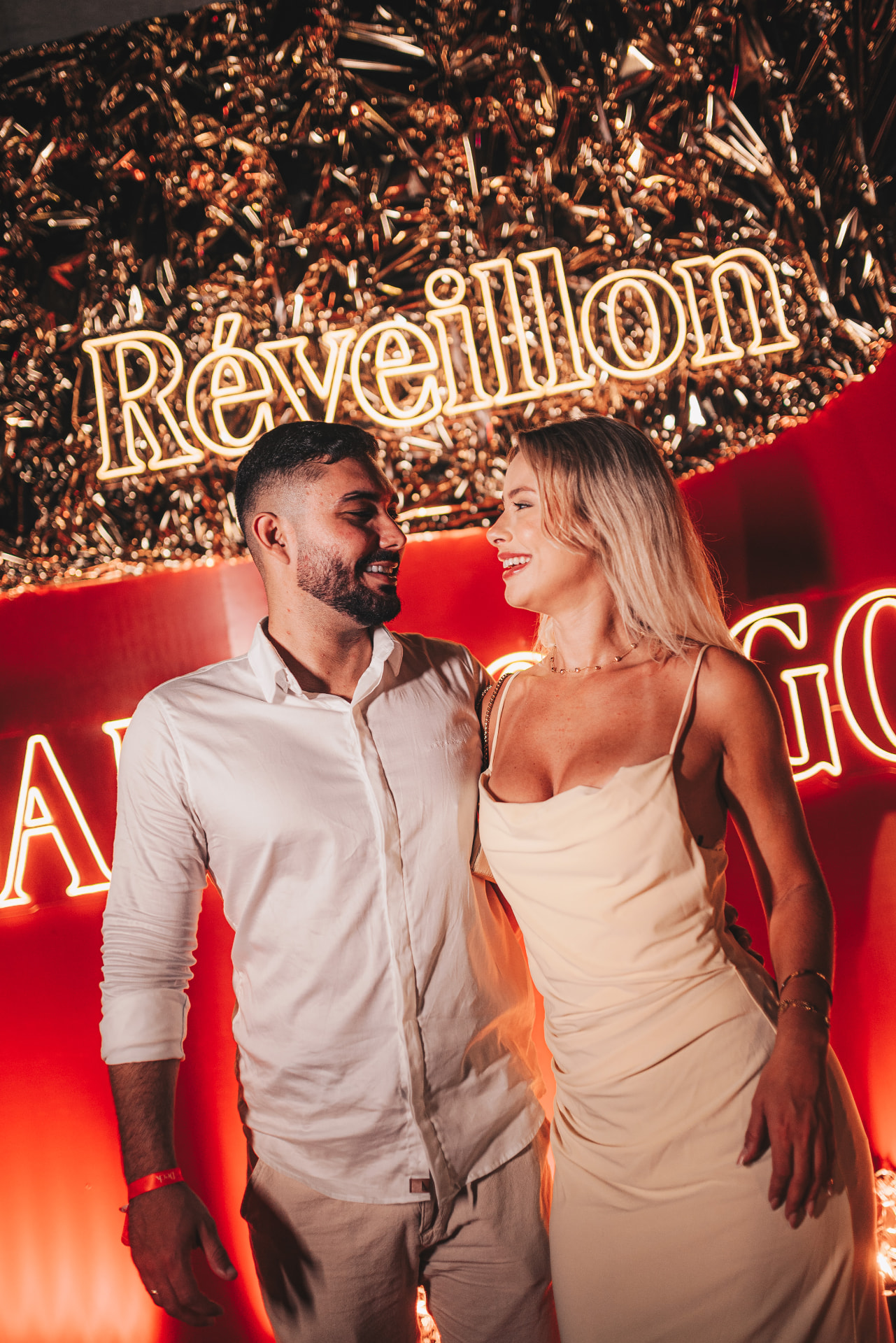 Casal sorrindo diante do letreiro luminoso do Réveillon do Golfe